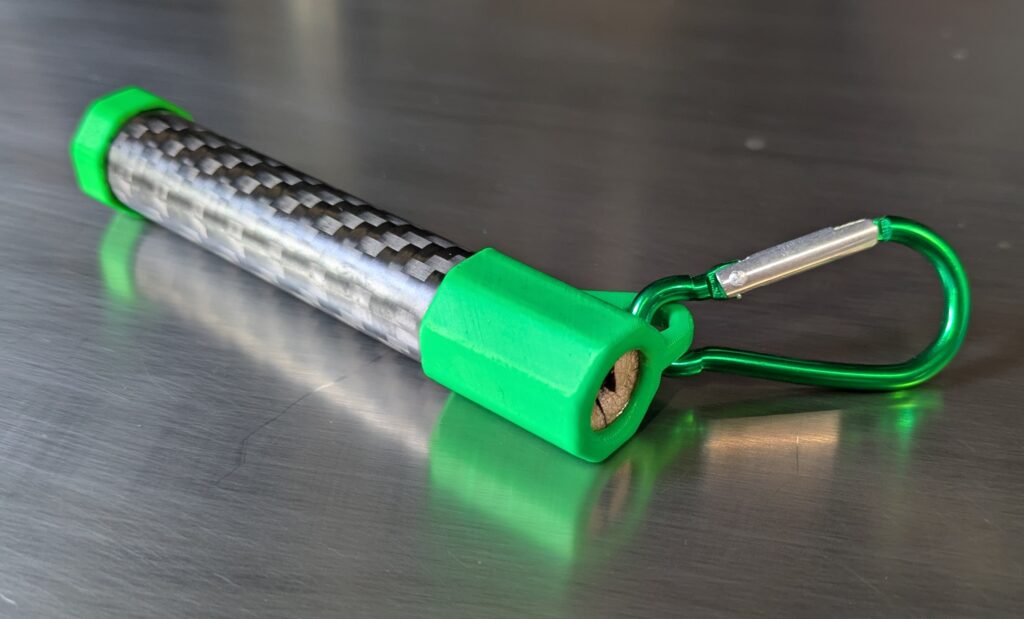 Green NockWorks SlyAro arrow lubricator pod with carbon-fibre tube and carabiner, shown horizontally